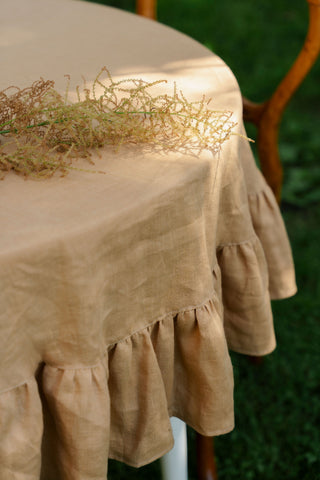 Tuvplāns: apaļa lina galdauta karameļu krāsā volāni un auduma tekstūra, dekorēts ar sausiem ziediem | Close-up of caramel linen tablecloth ruffles and fabric texture, decorated with dried flowers