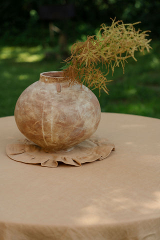 Māla vāze ar sausiem ziediem uz apaļa lina galdauta karameļu krāsā ar volāniem | Clay vase with dried flowers on a round caramel linen tablecloth with ruffles