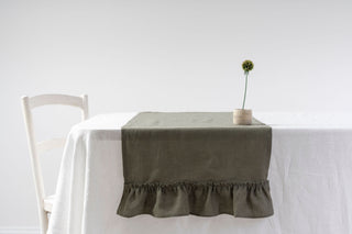 Olīvzaļš lina galda celiņš ar volāniem pa vidu galdam