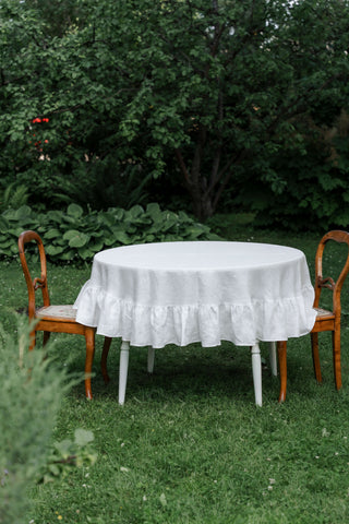 apaļš lina galdauts ar volāniem baltā krāsā dārzā ar retro krēsliem / round linen tablecloth with ruffle in white colour in garden with antique chairs