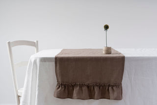 Brūns lina galda celiņš ar volāniem uz galda
