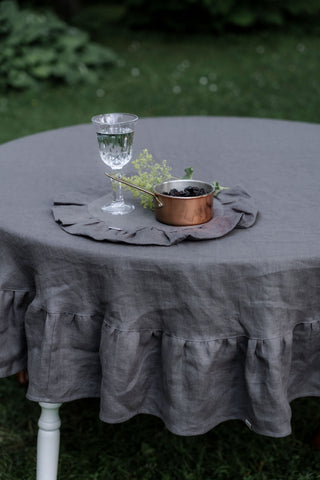 	Pelēks apaļš lina galdauts ar volāniem uz apaļa galda āra vidē, skats no augšas	Grey round linen tablecloth with ruffles on outdoor table, top view